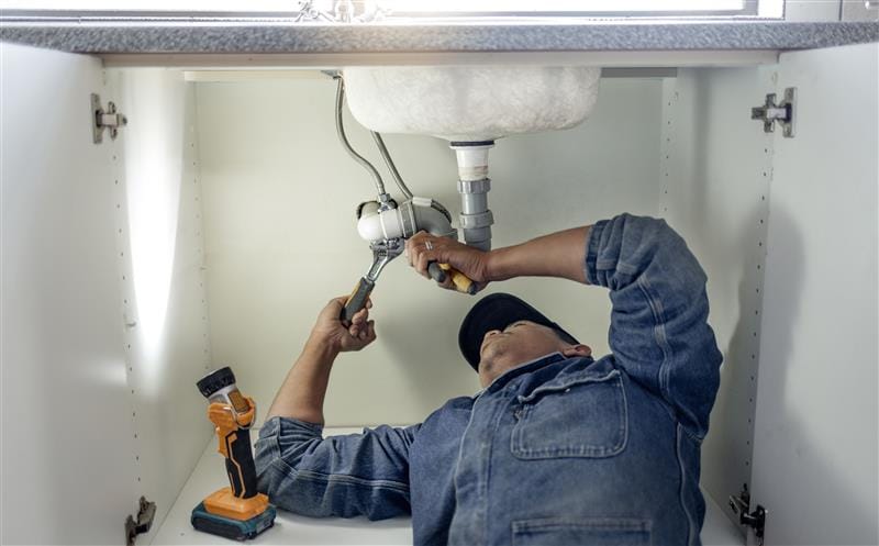 Plumber repairing pipes beneath a bathroom sink in Winter Park