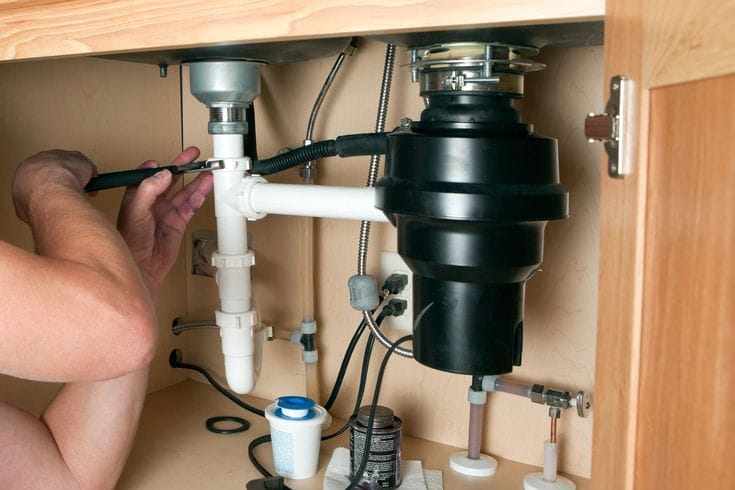 Plumber installing a garbage disposal beneath a kitchen sink in Winter Park