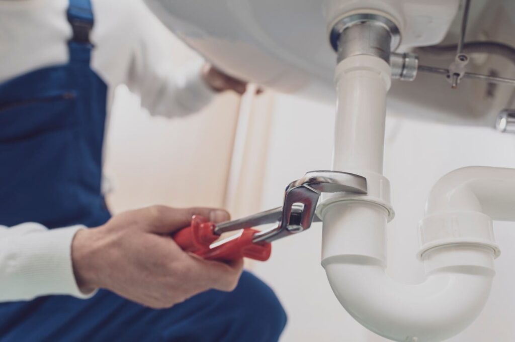 Plumber repairing a white drain pipe beneath a sink in Winter Park